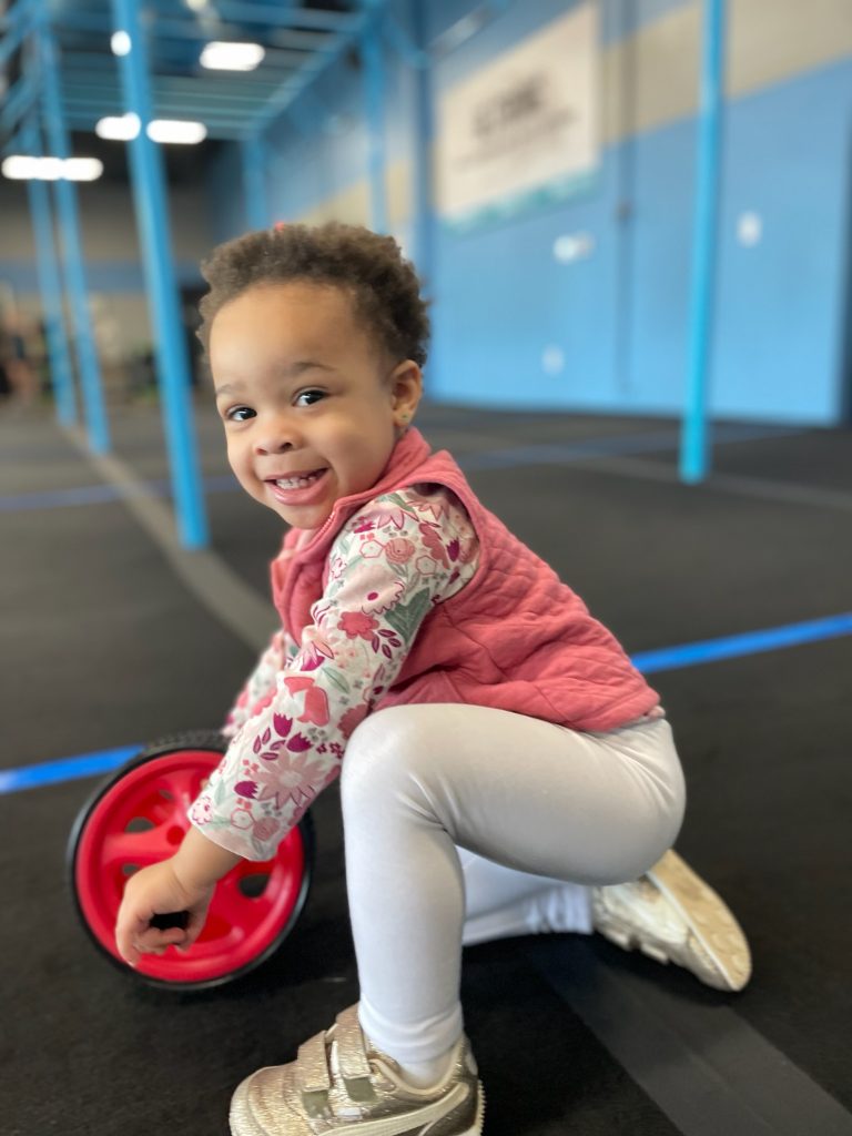 Toddler girl smiling with ab wheel exercise equipment have you ever wondered How our body image affects our kids