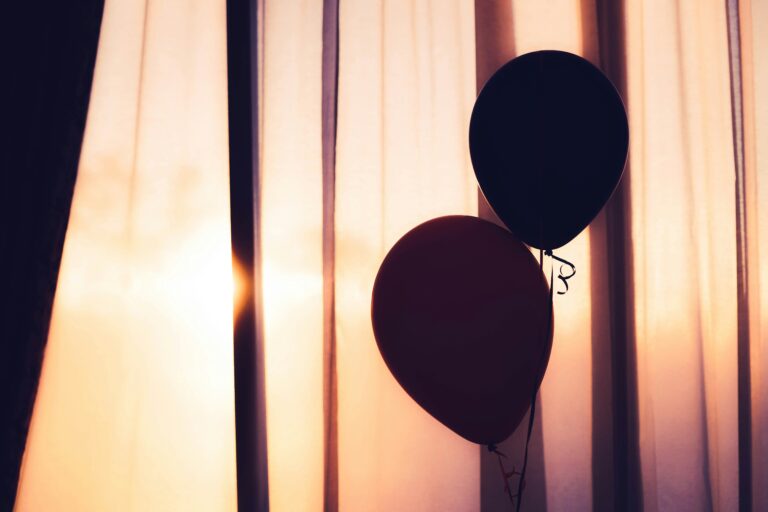 dimly lit birthday balloons in front of a curtain covering a sunset