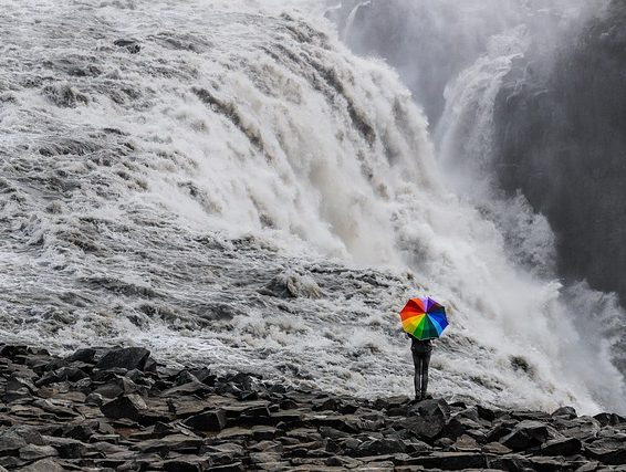 woman holding a rainbow umbrella in front of a waterfall supporting gender identity