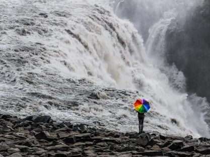 woman holding a rainbow umbrella in front of a waterfall supporting gender identity