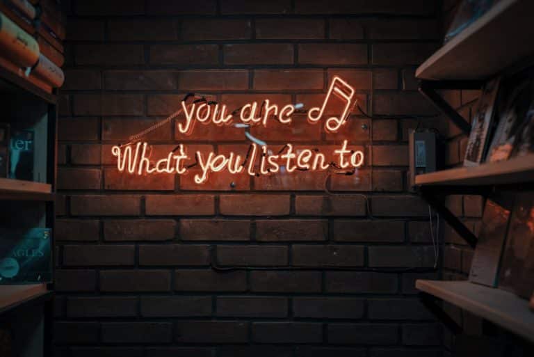 red neon letters spell out "you are what you listen to" on a brick background