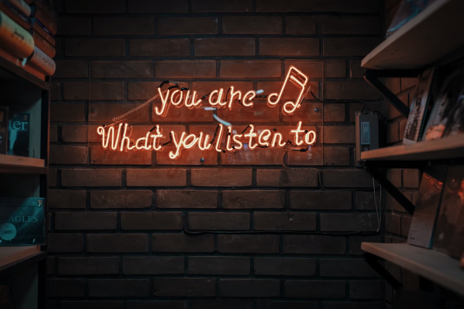 red neon letters spell out "you are what you listen to" on a brick background