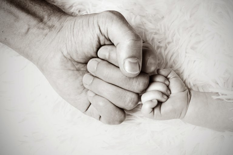 A black and white photo of an adult masculine hand and baby hand are fist bumping