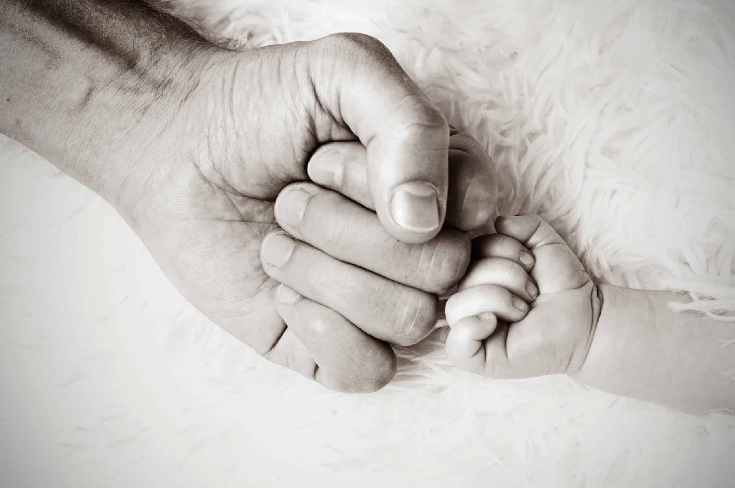 A black and white photo of an adult masculine hand and baby hand are fist bumping