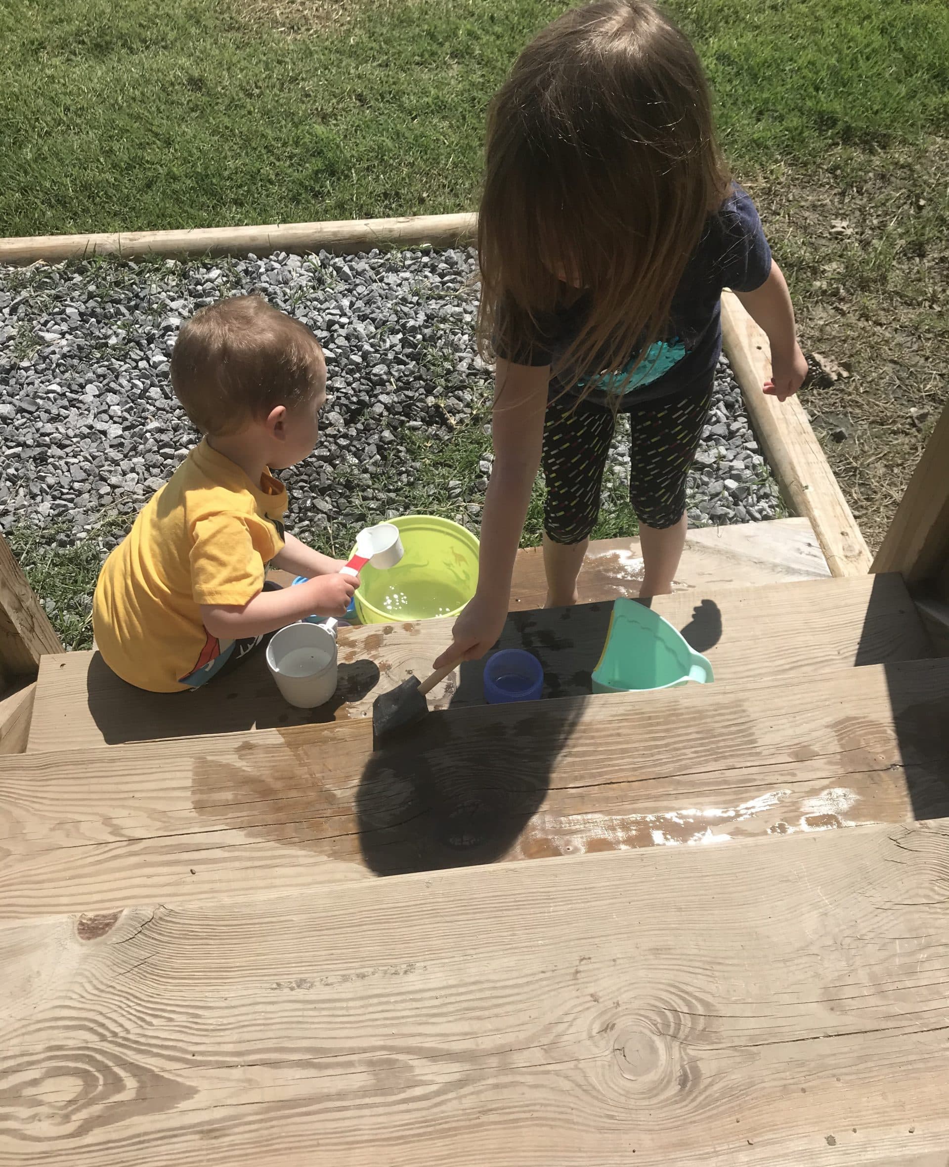 Two children using brushes to paint stairs with water.