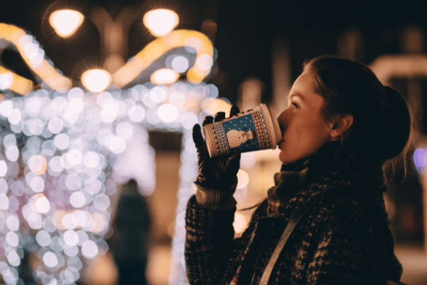 woman drinking coffee in front of Christmas lights