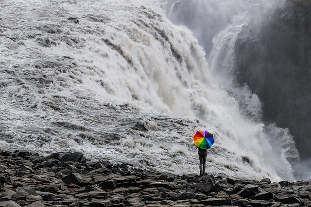woman holding a rainbow umbrella in front of a waterfall supporting gender identity