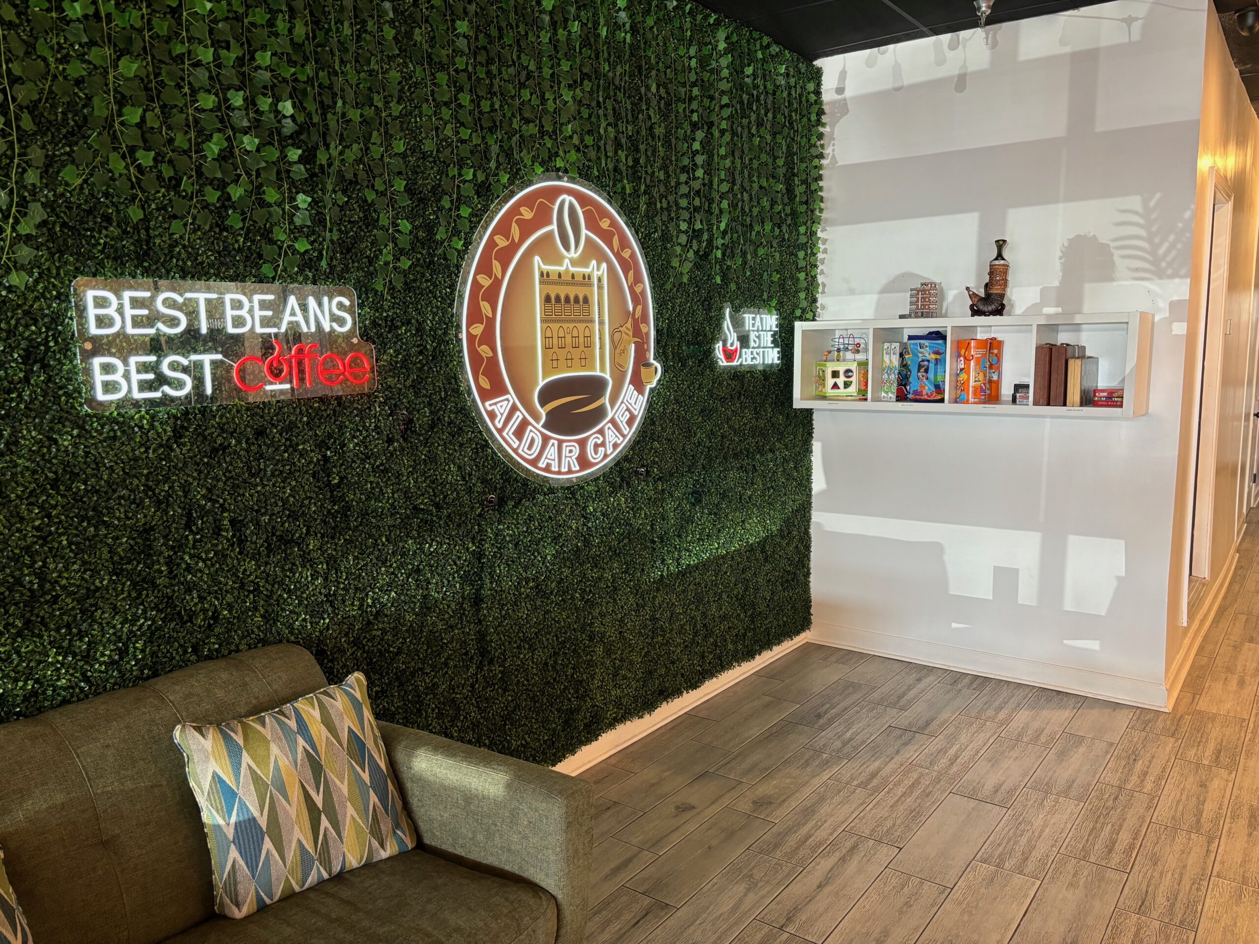 Game Corner shelf next to a green backdrop with Aldar Cafe Logo on it and a couch