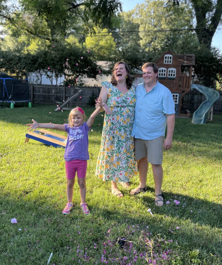 Couple and little girl looking at pink confetti that popped into the air.